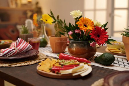 Bunch of various flowers in brown vase standing in the center of festive table served with appetizing snacks, fruits and other treats