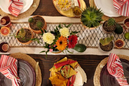 Top view of served festive table with domestic flowers in flowerpots, gerberas and carnations in vase and plates with napkins