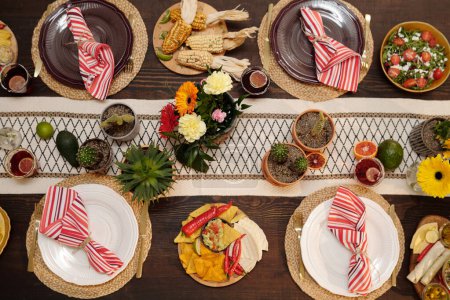 Foto de Vista superior de la mesa festiva con cactus en macetas y otras flores en jarrón, platos con servilletas, frutas, bebidas y aperitivos caseros - Imagen libre de derechos