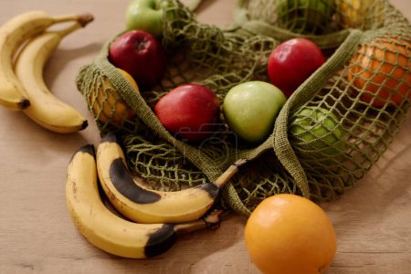 Foto de Parte de la bolsa de compras con variedad de frutas en la mesa, incluyendo plátanos en mal estado y frescos, naranjas maduras, manzanas rojas y verdes - Imagen libre de derechos