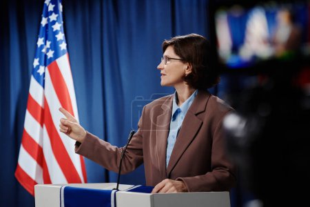 Téléchargez les photos : Femme mûre leader politique regardant son adversaire et le pointant du doigt tout en se tenant par la plate-forme et en exprimant son opinion - en image libre de droit