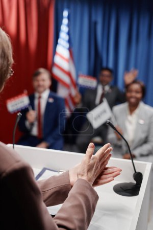 Foto de La política femenina hace un gesto convincente sobre la plataforma mientras habla frente al público intercultural sosteniendo banderas de votación en la conferencia - Imagen libre de derechos