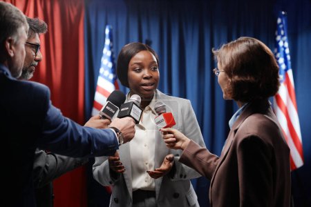 Foto de Joven mujer afroamericana explicando temas políticos mientras responde preguntas de periodistas con micrófonos en conferencia de prensa - Imagen libre de derechos