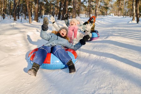 Téléchargez les photos : Groupe d'enfants joyeux en vêtements d'hiver criant tout en descendant la colline sur des tubes à neige et des glissières et en appréciant de passer du temps ensemble - en image libre de droit