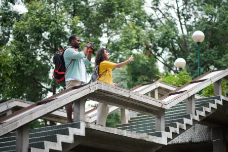 Téléchargez les photos : Jeune couple debout sur un grand escalier lors d'une excursion touristique et de la prise de photos de scènes naturelles et urbaines - en image libre de droit