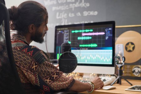Konzentrieren Sie sich auf junge indische Mann Blick auf Computerbildschirm mit Frequenzdiagramm der grafischen Audio-Equalizer, während die Erstellung von Musik zu Hause