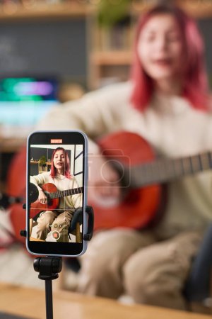 Foto de Teléfono móvil en trípode con adolescente en la pantalla de grabación de vídeo de la realización de nuevas canciones y tocar la guitarra para el público en línea - Imagen libre de derechos