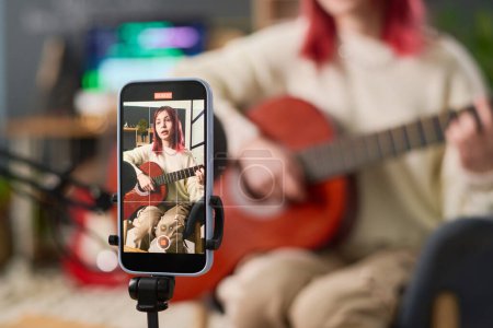 Bildschirm des Smartphones mit hübschen Teenager-Musiker während der Online-Lektion des Gitarrenspiels, Erstellen neuer Musik, Komponieren und Aufführen von Songs