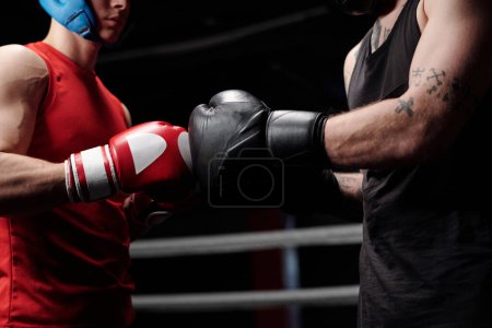 Recortado tiro de dos jóvenes boxeadores musculosos en ropa deportiva tocando por sus manos en guantes de boxeo antes de comenzar la ronda de sparring