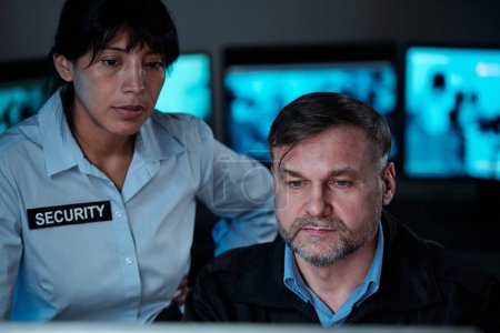 Photo for Two serious security guards looking at computer screen in control room while observing situation in supermarket or some other building - Royalty Free Image