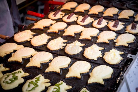 Téléchargez les photos : Délicieux taiyaki : Pâtisserie en forme de poisson remplie de haricots rouges et de thé vert. Un régal japonais populaire cuit sur une poêle en fer. - en image libre de droit