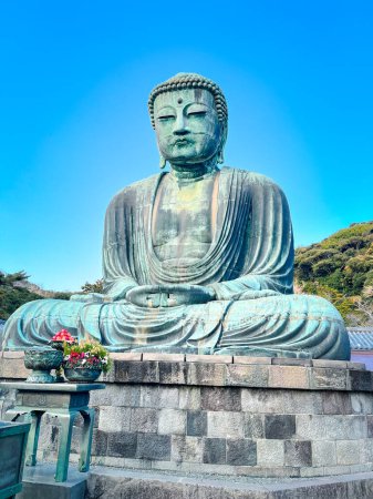 Eine große Buddha-Statue, die in einem Kamakura sitzt. Die Statue ist von Bäumen und einem Gebäude umgeben