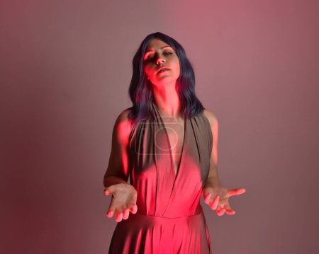 portrait of pretty girl with blue hair,  gestural arm pose reaching into colourful light source. colourful neon gel lighting, isolated on studio background.