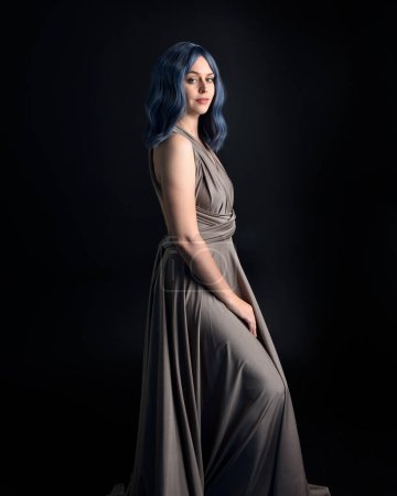 portrait of pretty girl with blue hair wig & elegant gown with expressive facial expressions & gestural arm poses. colourful neon gel lighting, isolated on studio background.