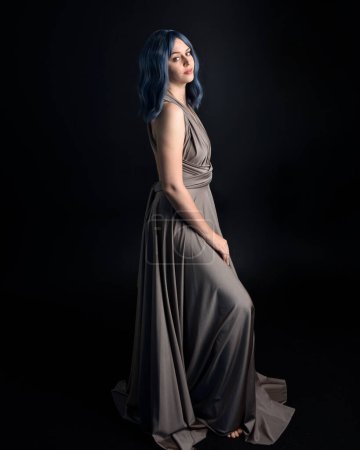portrait of pretty girl with blue hair wig & elegant gown with expressive facial expressions & gestural arm poses. colourful neon gel lighting, isolated on studio background.