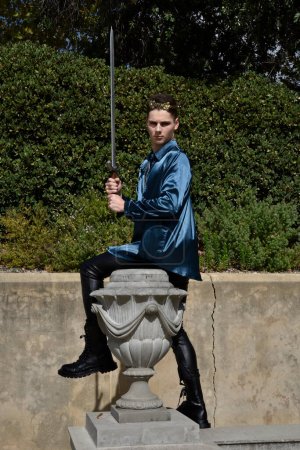  portrait of handsome brunette male model wearing fantasy medieval prince costume, romantic silk shirt, holding sword weapon.  historical castle location background with stone staircase.