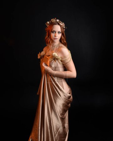 Photo for Close up fantasy portrait of beautiful woman model with red hair, goddess silk robes & ornate gold crown.  Posing with gestural hands reaching out, isolated on dark  studio background - Royalty Free Image