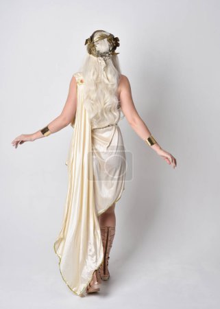 Portrait complet de belle femme blonde portant un costume de toge déesse fantaisie avec couronne magique.Pose debout, face à l'arrière loin de la caméra. isolé sur fond de studio blanc.