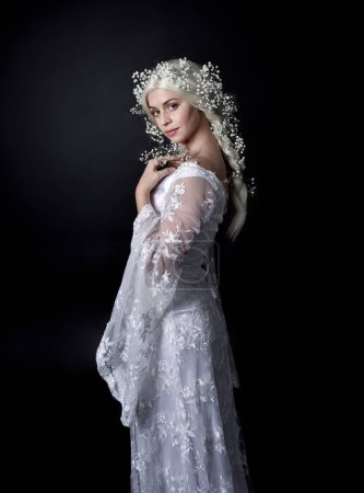 Close up portrait of beautiful women with long blonde hair, wearing white fantasy princess ball gown, holding pretty baby breath flowers, isolated on black studio background