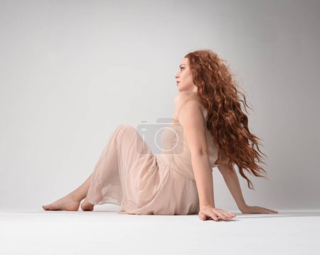 Photo for Full length portrait of beautiful brunette model  wearing a  pink dress. graceful sitting  pose, kneeling on floor gestural hands. shot from low angle perspective,  isolated on white studio background. - Royalty Free Image