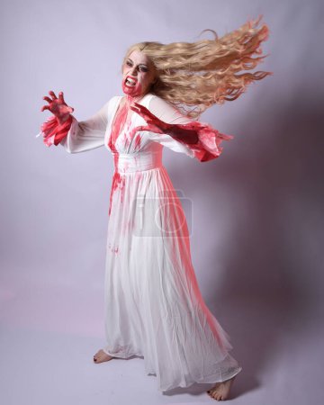  Full length portrait of  scary vampire zombie bride, wearing elegant halloween fantasy costume  dress with bloody red paint splatter. standing walking pose. Isolated on white studio background 