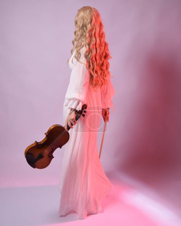 Photo for Full length portrait of beautiful blonde model wearing elegant white halloween gown, historical fantasy character.  facing backwards holding a violin musical instrument, isolated on studio background. - Royalty Free Image