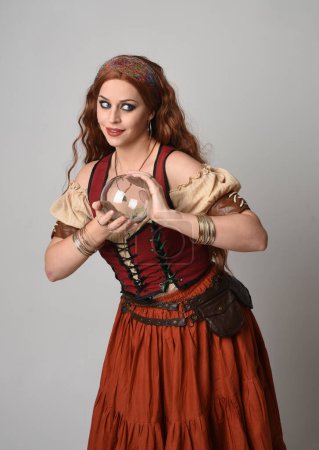 Photo for Close up portrait of beautiful red haired woman wearing a medieval maiden, fortune teller costume. Posing while  holding a  crystal ball. isolated on studio background. - Royalty Free Image