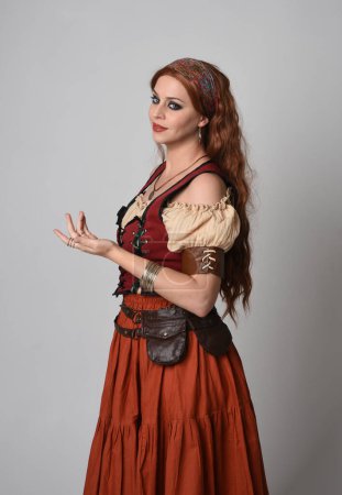 Photo for Close up portrait of beautiful red haired woman wearing a medieval maiden, fortune teller costume. Posing with gestural hands reaching out, dancing, isolated on studio background. - Royalty Free Image