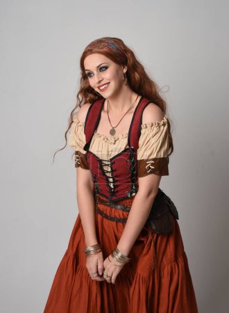 Photo for Close up portrait of beautiful red haired woman wearing a medieval maiden, fortune teller costume. Posing with gestural hands reaching out, dancing, isolated on studio background. - Royalty Free Image