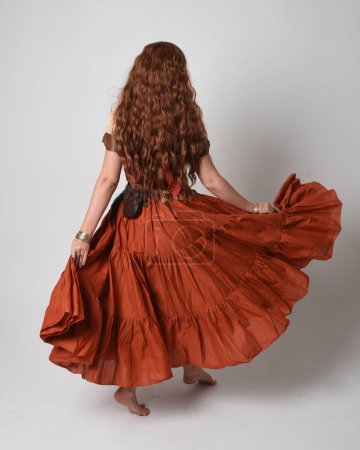 Photo for Full length portrait of beautiful red haired woman wearing a medieval maiden, fortune teller costume. Standing pose back view, walking away. isolated on studio background. - Royalty Free Image