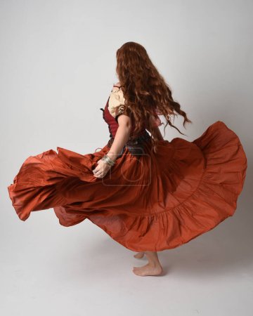 Full length portrait of beautiful red haired woman wearing a medieval maiden, fortune teller costume. Standing pose back view, walking away. isolated on studio background.