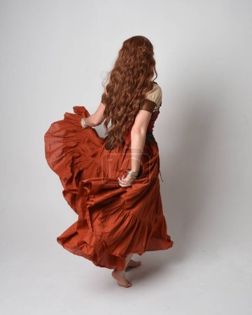 Retrato de cuerpo entero de una hermosa mujer pelirroja vestida con una doncella medieval, disfraz de adivina. Posar de pie vista trasera, alejándose. aislado en el fondo del estudio.