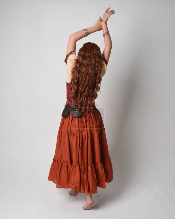 Photo for Full length portrait of beautiful red haired woman wearing a medieval maiden, fortune teller costume. Standing pose back view, walking away. isolated on studio background. - Royalty Free Image