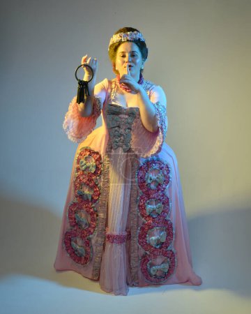Photo for Cinematic  portrait of female model wearing an opulent pink gown,  costume of a historical French baroque nobility, style of Marie Antoinette. Holding ring of keys,  Isolated on  studio background - Royalty Free Image