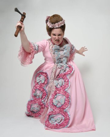 Porträt eines weiblichen Modells in opulentem rosa Kleid, Kostüm eines historischen französischen Barockadels, Stil von Marie Antoinette. Axt Waffe in revolutionärer Angriffspose. Studiohintergrund