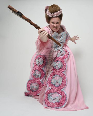 Porträt eines weiblichen Modells in opulentem rosa Kleid, Kostüm eines historischen französischen Barockadels, Stil von Marie Antoinette. Axt Waffe in revolutionärer Angriffspose. Studiohintergrund