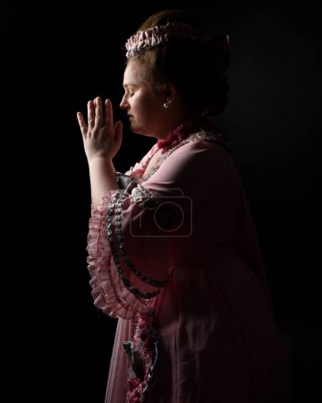 Nahaufnahme Porträt eines weiblichen Modells in einem opulenten rosafarbenen Kleid, Kostüm eines historischen französischen Barockadels im Stil von Marie Antoinette. Isolierte dunkle filmische Silhouette Studiohintergrund