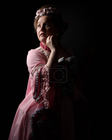 close upProfile portrait of female model wearing an opulent pink gown, costume of a historical French baroque nobility, style of Marie Antoinette. Isolated dark cinematic silhouette studio background