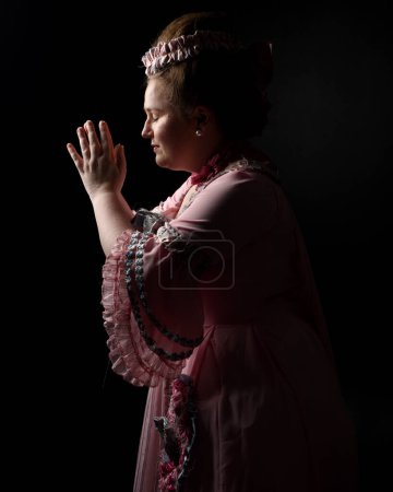 Foto de Close upRetrato de perfil de modelo femenina con un vestido rosa opulento, traje de una nobleza barroca francesa histórica, estilo de María Antonieta. Fondo de estudio de silueta cinematográfica oscura aislada - Imagen libre de derechos