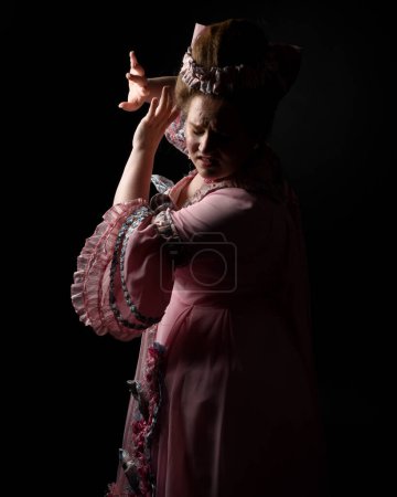 Photo for Close upProfile portrait of female model wearing an opulent pink gown, costume of a historical French baroque nobility, style of Marie Antoinette. Isolated dark cinematic silhouette studio background - Royalty Free Image