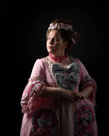 Foto de Close upRetrato de perfil de modelo femenina con un vestido rosa opulento, traje de una nobleza barroca francesa histórica, estilo de María Antonieta. Fondo de estudio de silueta cinematográfica oscura aislada - Imagen libre de derechos