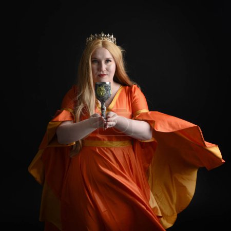 primer plano retrato de mujer rubia de tamaño grande, con vestido de fantasía medieval histórica, reina real coronada. posando sosteniendo copa de vino bebiendo copa, aislado negro oscuro fondo del estudio.