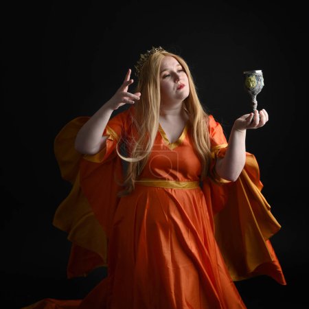 primer plano retrato de mujer rubia de tamaño grande, con vestido de fantasía medieval histórica, reina real coronada. posando sosteniendo copa de vino bebiendo copa, aislado negro oscuro fondo del estudio.