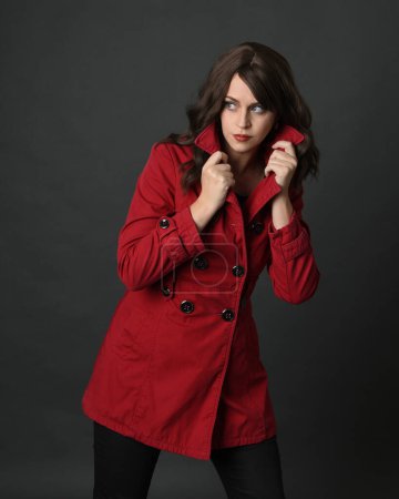 Nahaufnahme Porträt der schönen brünetten Frau Modell, trägt roten Trenchcoat jacket.isolated auf dunklem Studiohintergrund mit Schatten. Halsband in geheimnisvoller Versteckpose.