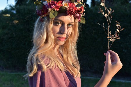 Photo for Close up portrait of pretty blonde female model wearing a flower crown wreath and purple dress.  green nature  plants and trees in background - Royalty Free Image
