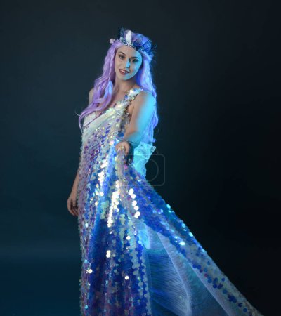Photo for Artistic portrait of beautiful female model with long purple hair wearing a fantasy fairy crown, wearing a rainbow glitter sequin ball gown. gestural flowing pose, isolated on dark studio background. - Royalty Free Image
