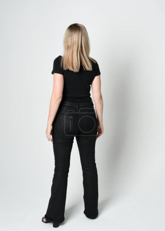 Ganzkörperporträt einer schönen blonden Frau in modernem schwarzen Hemd und Lederhose. Selbstbewusst im Stehen vor der Kamera, Silhouette auf weißem Studiohintergrund.