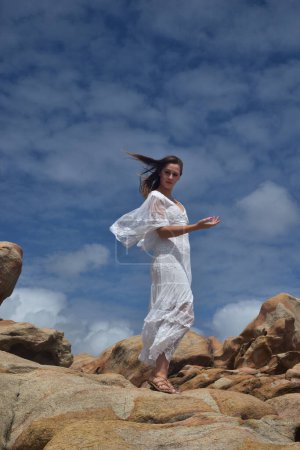 Porträt eines weiblichen Modells, das ein weißes Göttinnenkleid trägt, dramatische Naturlandschaft mit felsigem Meeresufer und steinernen Klippen. Burgfelsen, Busselton, Westaustralien