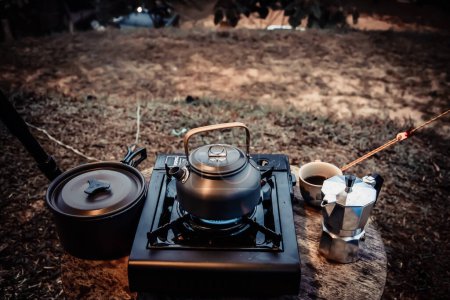 Photo for Outdoor kitchen equipment camp fire and brewing tea pot moka coffee drip cup,with wooden table camping gas stove set in nature outdoor,mountain background,concept camp and travel,vintage tone color - Royalty Free Image