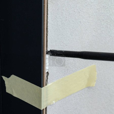 Téléchargez les photos : The use of painter's tape in the installation of the door, the tape restrains the deformation of the door during the filling of the gaps between the door and the wall with foam, repairs. - en image libre de droit